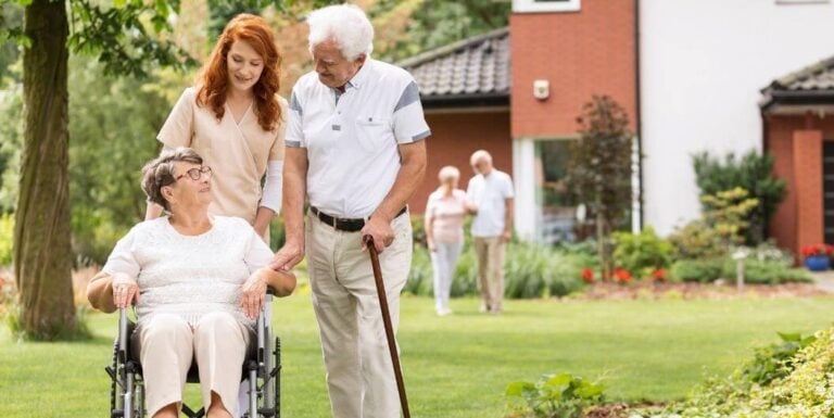 Elderly Woman in Wheelchair Smiling with Nurse at Memory Care Facility