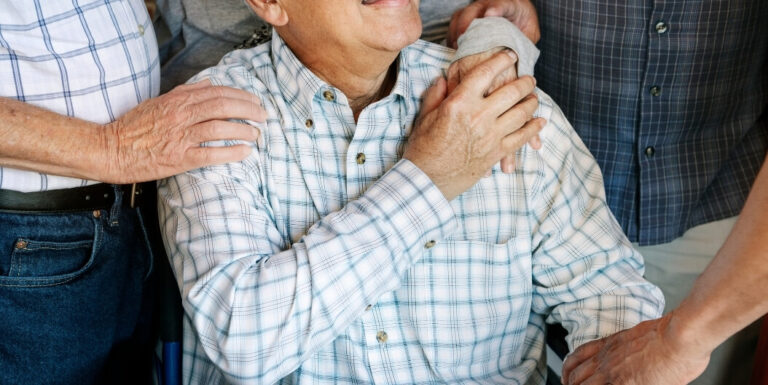 Elderly Man Comforted by Friends With Hands on Shoulder in Memory Care