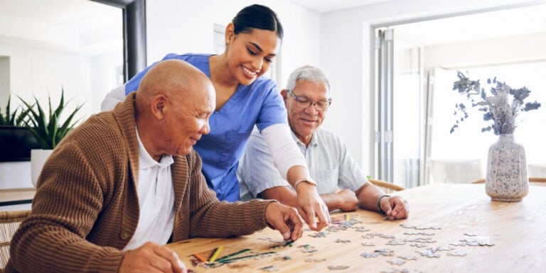 Female Nurse Assisting Elderly Male Residents with a Puzzle at a Memory Care Facility